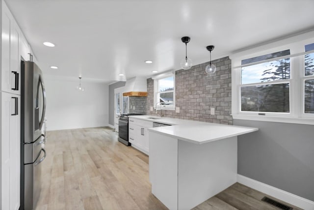 kitchen with kitchen peninsula, tasteful backsplash, stainless steel appliances, white cabinets, and hanging light fixtures