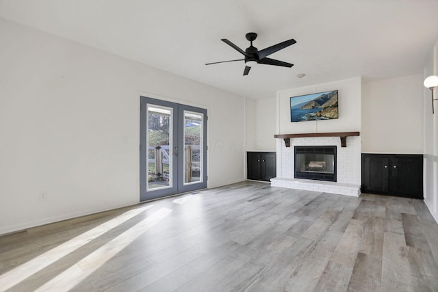 unfurnished living room featuring ceiling fan, french doors, light hardwood / wood-style flooring, and a brick fireplace