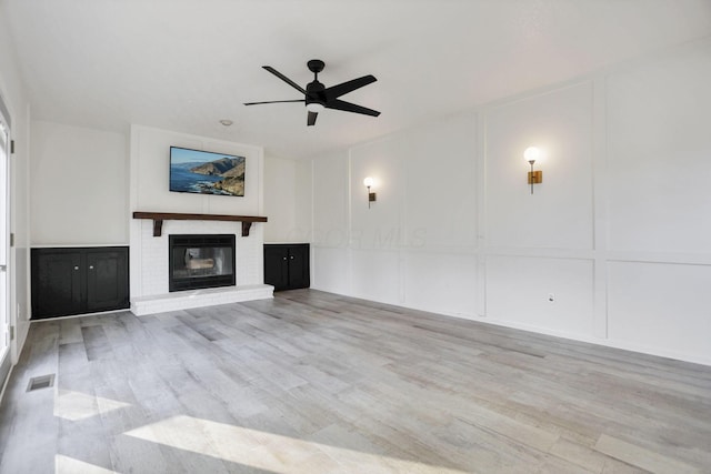 unfurnished living room with ceiling fan, light hardwood / wood-style flooring, and a brick fireplace