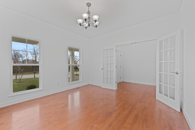 spare room with french doors, a chandelier, and light wood-type flooring