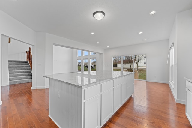 kitchen with light hardwood / wood-style floors, a center island, light stone counters, and white cabinetry