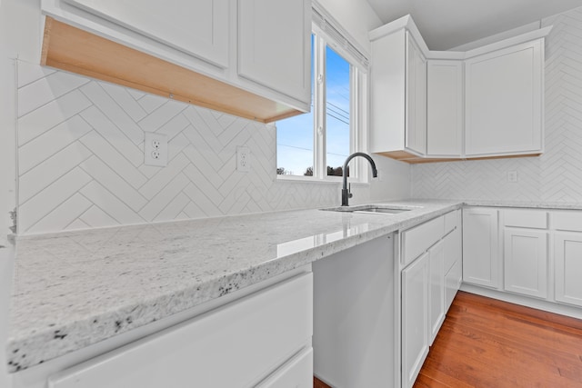 kitchen featuring light stone countertops, light wood-type flooring, backsplash, sink, and white cabinetry