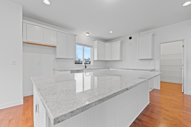 kitchen with a kitchen island, light stone counters, light hardwood / wood-style flooring, backsplash, and white cabinets