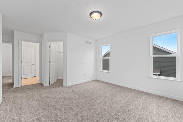 unfurnished bedroom with carpet flooring, a walk in closet, and multiple windows