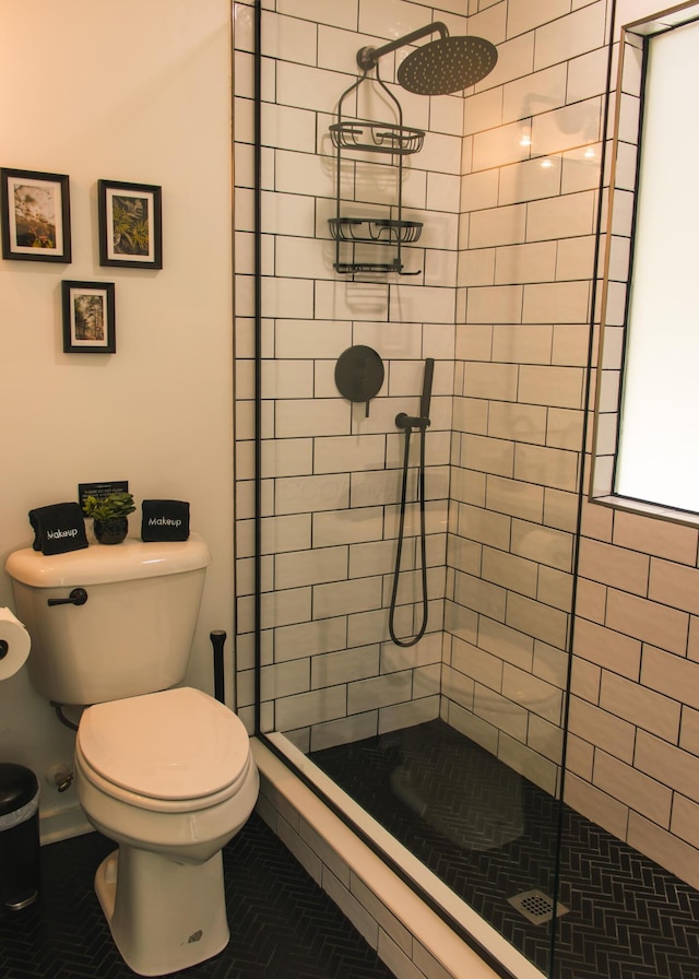 bathroom with a tile shower, toilet, and tile patterned floors