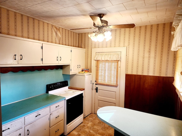 kitchen with ceiling fan, wood walls, white cabinetry, and white electric stove