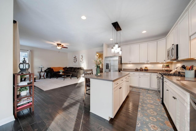 kitchen with appliances with stainless steel finishes, dark hardwood / wood-style flooring, a kitchen island, pendant lighting, and white cabinets