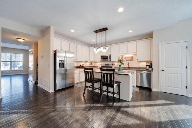 kitchen with appliances with stainless steel finishes, a center island, pendant lighting, and white cabinets