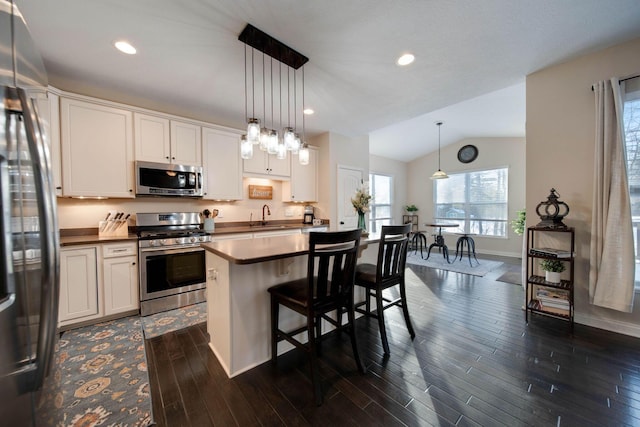 kitchen featuring a kitchen island, appliances with stainless steel finishes, pendant lighting, white cabinetry, and a kitchen breakfast bar