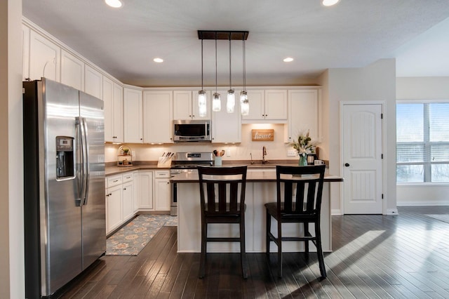 kitchen with a breakfast bar, white cabinetry, stainless steel appliances, a kitchen island, and decorative light fixtures