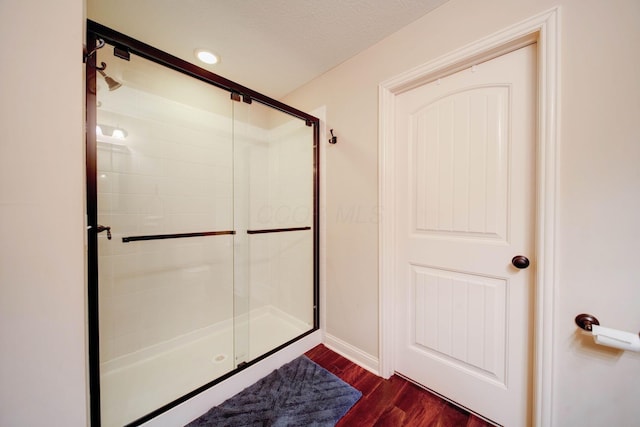 bathroom with wood-type flooring, a shower with door, and a textured ceiling