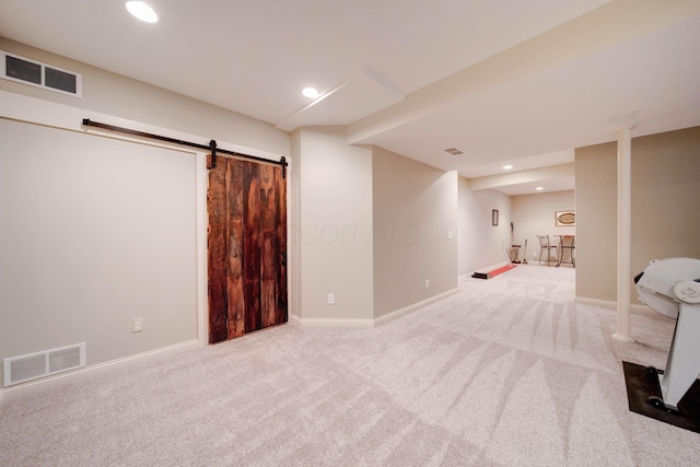 basement with a barn door and light colored carpet