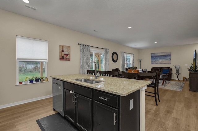 kitchen with light stone countertops, sink, light hardwood / wood-style flooring, stainless steel dishwasher, and an island with sink