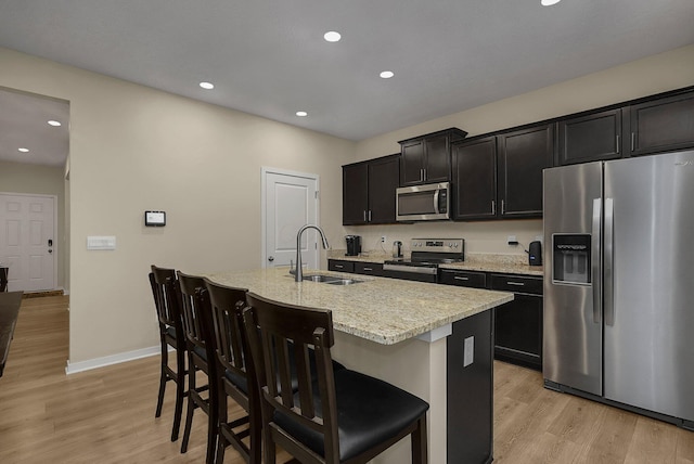 kitchen featuring stainless steel appliances, sink, a center island with sink, light hardwood / wood-style floors, and a breakfast bar area