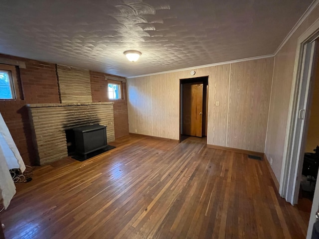 unfurnished living room featuring a textured ceiling, a wood stove, dark hardwood / wood-style floors, and ornamental molding