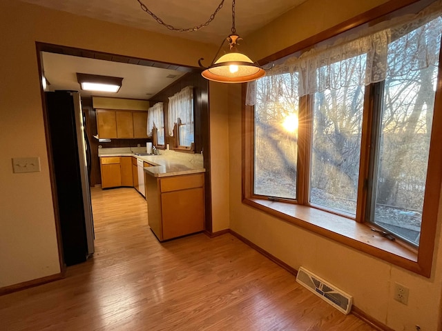 kitchen with light wood-type flooring, white dishwasher, stainless steel refrigerator, and plenty of natural light