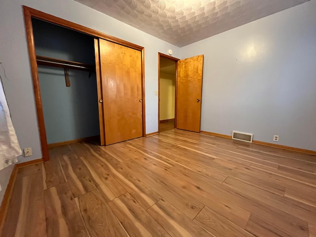 unfurnished bedroom featuring a textured ceiling, light hardwood / wood-style floors, and a closet