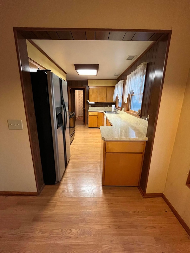 kitchen with sink, stainless steel fridge, light wood-type flooring, light stone counters, and kitchen peninsula