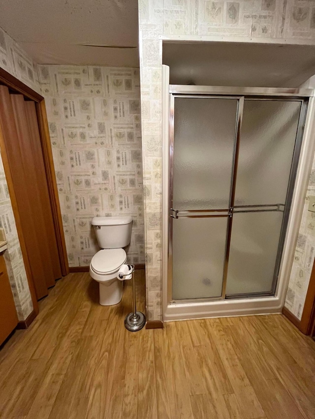 bathroom with hardwood / wood-style floors, toilet, and a shower with shower door