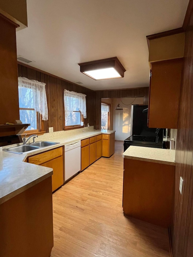 kitchen with wood walls, white dishwasher, sink, light hardwood / wood-style floors, and kitchen peninsula