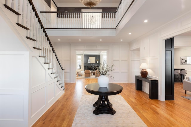 foyer with crown molding, a towering ceiling, and light hardwood / wood-style flooring