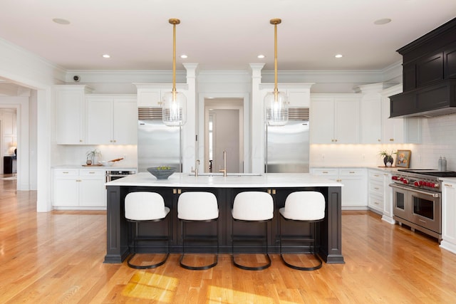 kitchen featuring sink, premium appliances, white cabinets, a center island with sink, and decorative light fixtures