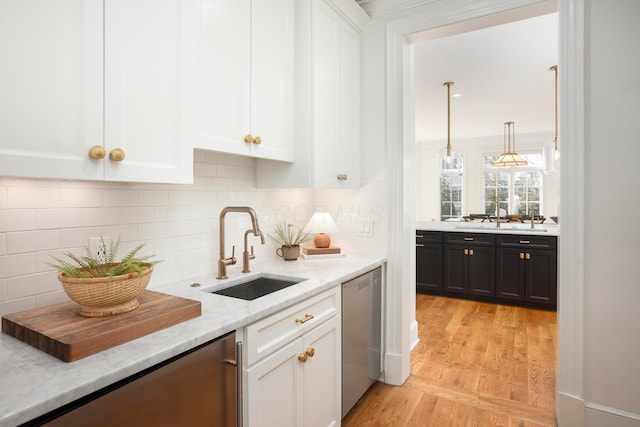 kitchen with white cabinetry, sink, hanging light fixtures, stainless steel dishwasher, and light stone countertops