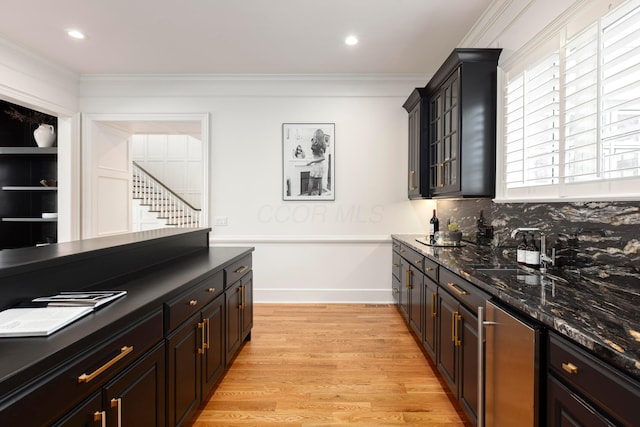 kitchen featuring sink, tasteful backsplash, ornamental molding, dark stone counters, and light hardwood / wood-style floors