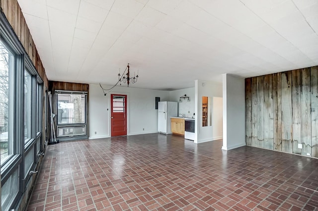 unfurnished living room featuring a notable chandelier and wood walls