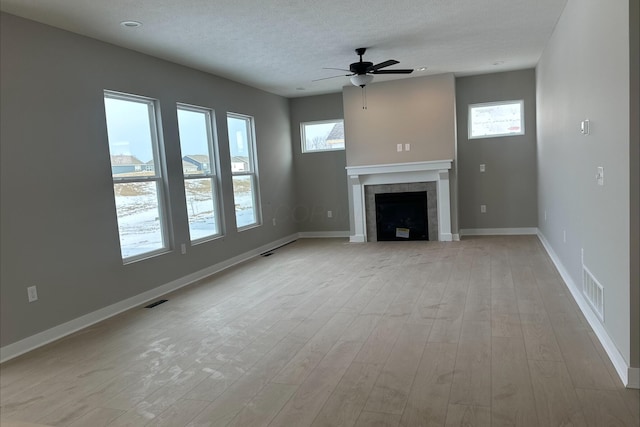 unfurnished living room with a tiled fireplace, ceiling fan, a textured ceiling, and light wood-type flooring