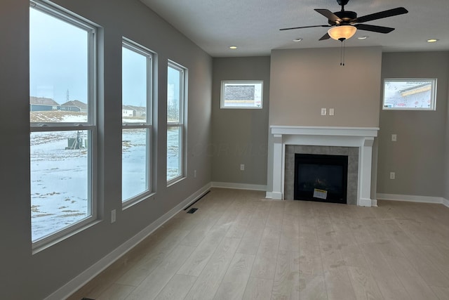 unfurnished living room with ceiling fan, light wood-type flooring, a textured ceiling, and a fireplace