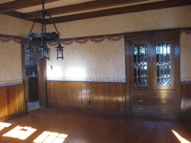 unfurnished dining area with beamed ceiling, dark hardwood / wood-style flooring, and wooden walls