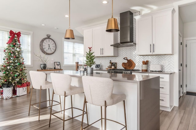 kitchen featuring white cabinetry, light hardwood / wood-style flooring, an island with sink, and wall chimney range hood