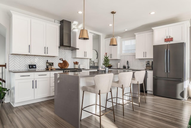 kitchen featuring a center island, hanging light fixtures, wall chimney range hood, white cabinets, and appliances with stainless steel finishes