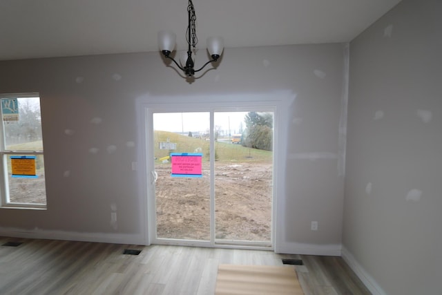 unfurnished dining area with an inviting chandelier, plenty of natural light, and light hardwood / wood-style flooring