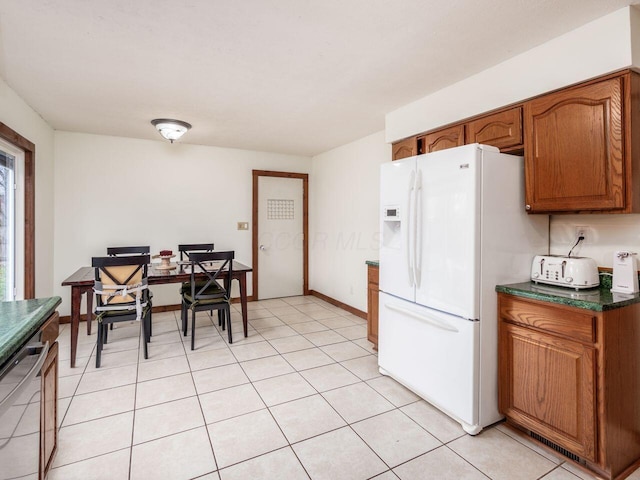 kitchen with light tile patterned floors, stainless steel dishwasher, and white refrigerator with ice dispenser