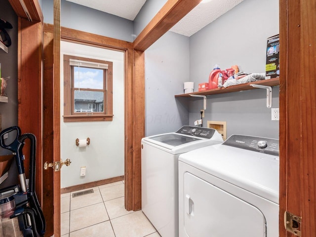 laundry area featuring washer and dryer, light tile patterned floors, and a textured ceiling