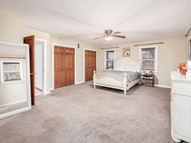 unfurnished bedroom featuring carpet, ceiling fan, a textured ceiling, and multiple closets