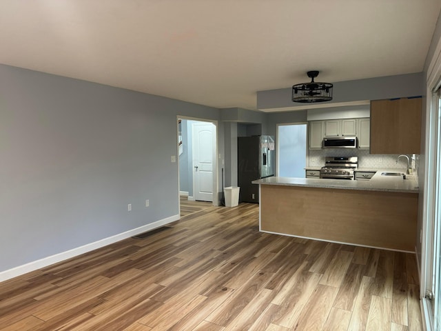 kitchen with sink, stainless steel appliances, backsplash, kitchen peninsula, and hardwood / wood-style flooring