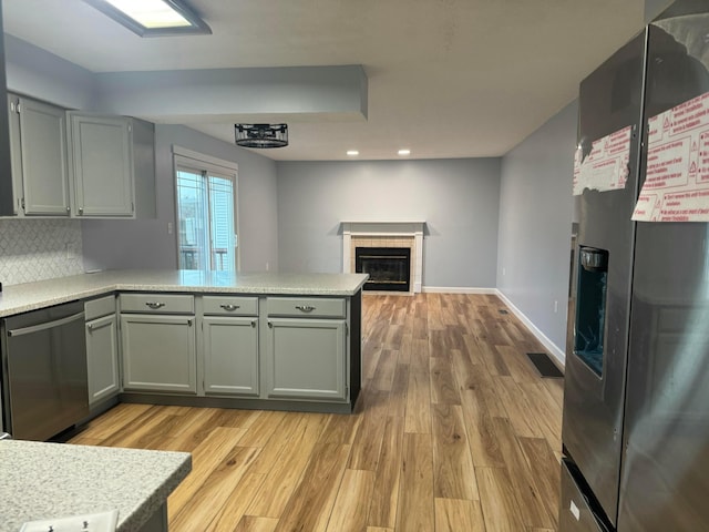 kitchen featuring kitchen peninsula, appliances with stainless steel finishes, gray cabinets, light hardwood / wood-style floors, and a tiled fireplace