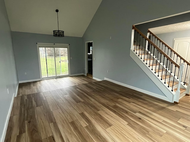 unfurnished living room with high vaulted ceiling, wood-type flooring, and an inviting chandelier