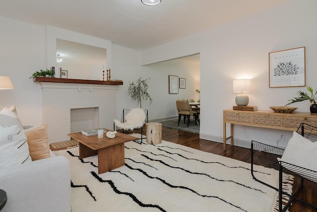 living room featuring dark wood-type flooring and a brick fireplace