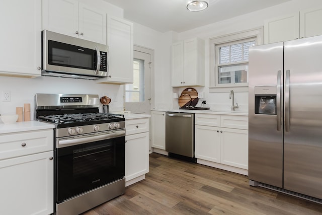 kitchen with appliances with stainless steel finishes, dark hardwood / wood-style flooring, white cabinetry, and a healthy amount of sunlight