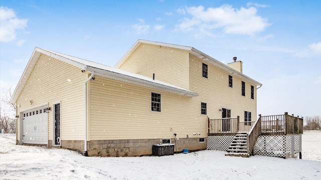 snow covered house featuring central air condition unit, a deck, and a garage