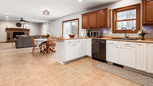 kitchen featuring ceiling fan, dishwasher, sink, kitchen peninsula, and a fireplace