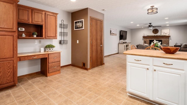 kitchen featuring a textured ceiling, ceiling fan, white cabinets, and a fireplace