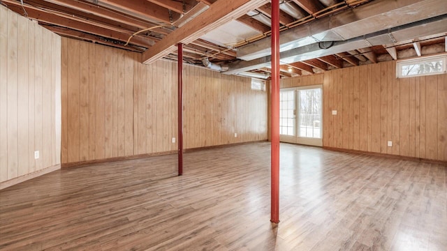 basement featuring a healthy amount of sunlight, wood-type flooring, and wooden walls