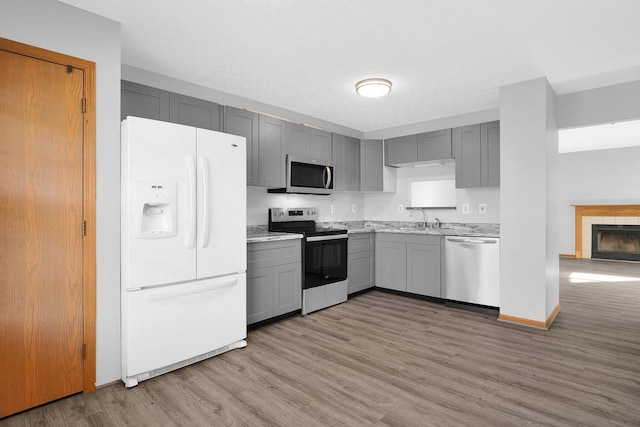 kitchen with a tile fireplace, gray cabinetry, stainless steel appliances, and light wood-type flooring