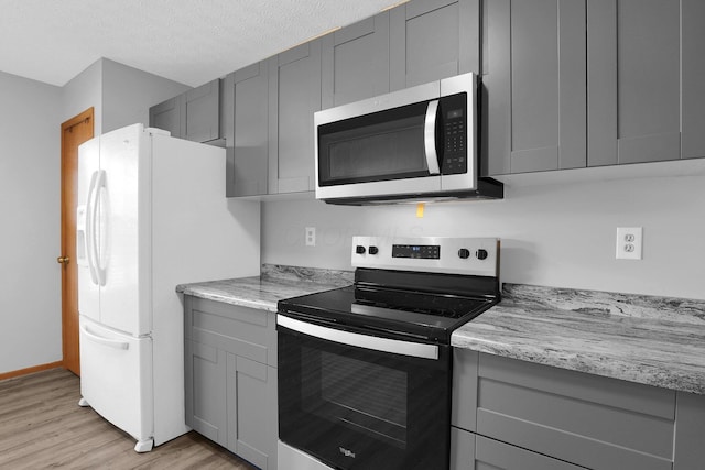 kitchen featuring gray cabinetry, light stone countertops, a textured ceiling, light hardwood / wood-style floors, and stainless steel appliances