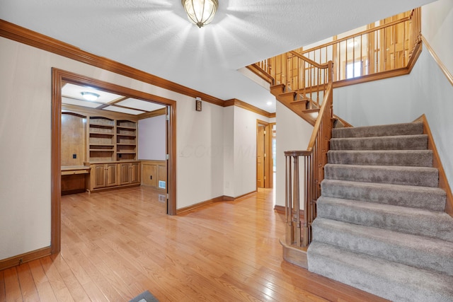 staircase featuring hardwood / wood-style floors, a textured ceiling, built in features, and crown molding